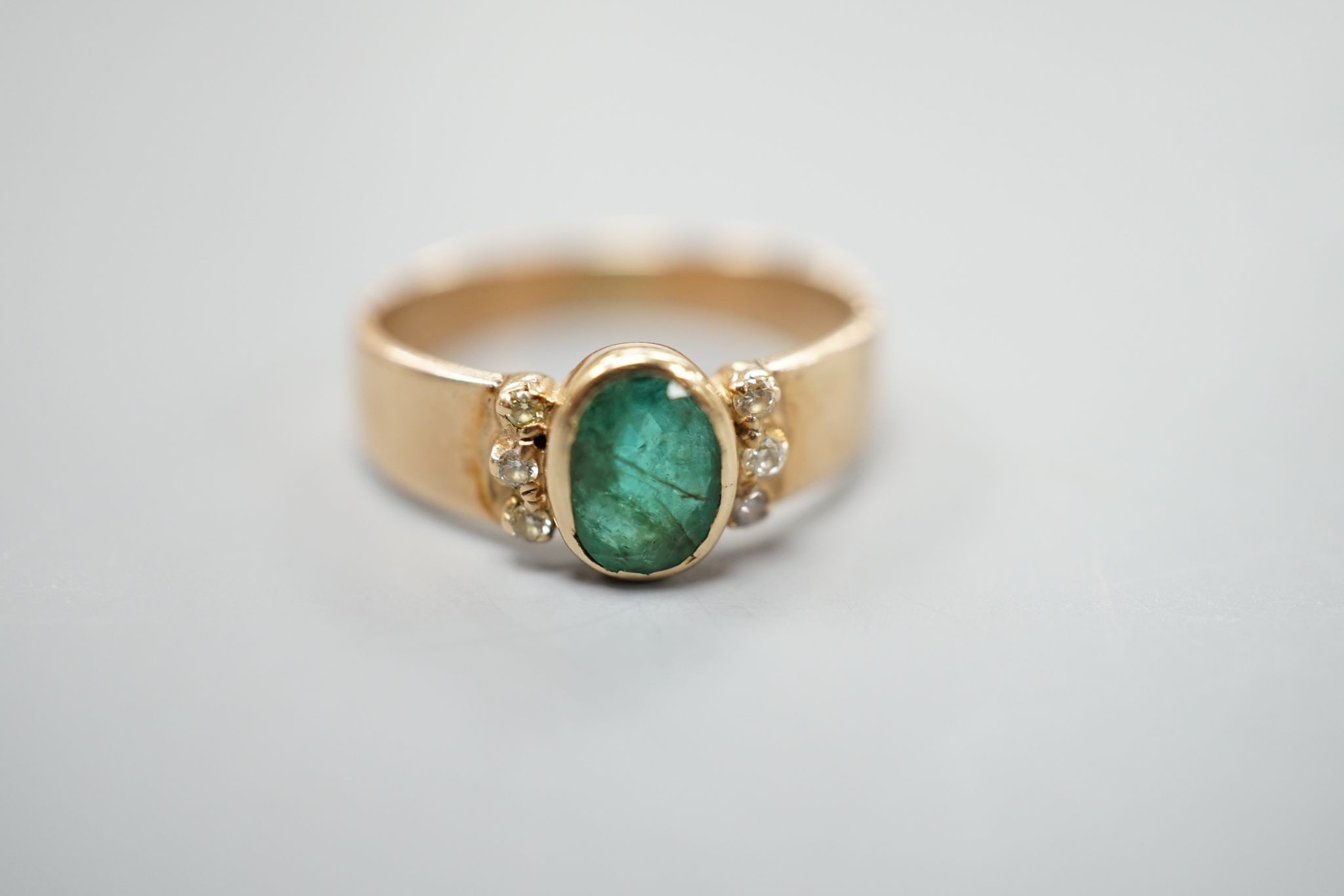 A yellow metal, oval cut emerald and six stone diamond chip set ring, size O, gross weight 3 grams.